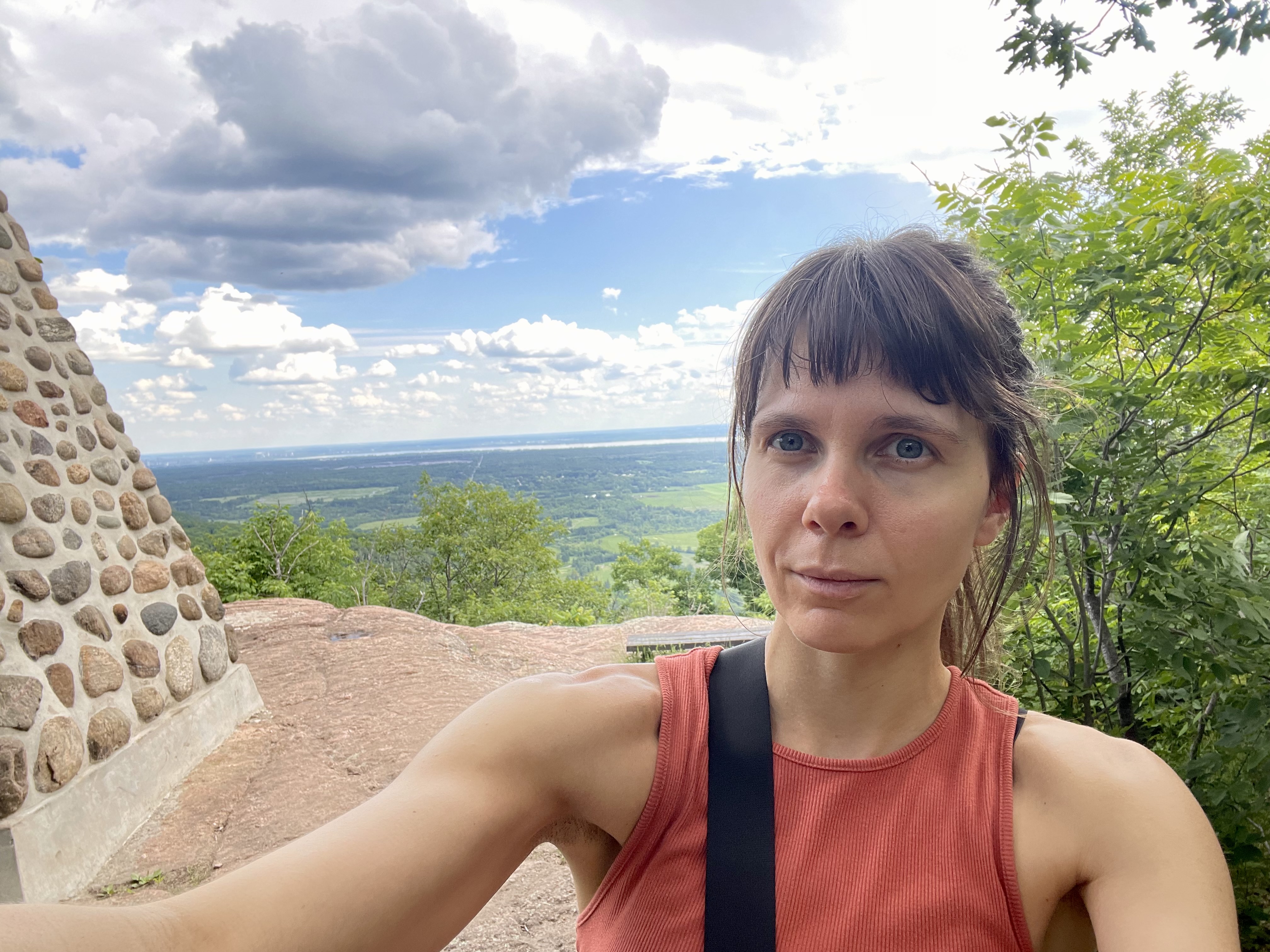 Rozalia Rozzebud Kieliszkiewicz outdoors at a scenic mountain lookout surrounded by trees and open sky